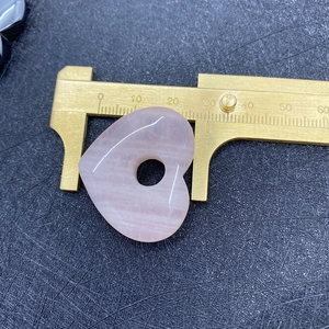 Detailopname van rozenkwarts hart hanger gemeten met een gouden schuifmaat voor de maat