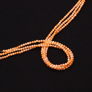 Macro-detail van drie strengen oranje schelpkralen met natuurlijke glans op zwarte basis