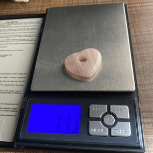 Macro-opname van een hartvormige rozenkwarts hanger van 11,3 g op een digitale weegschaal