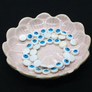 Close-up of shell beads with blue Evil Eye design on a pink ceramic plate