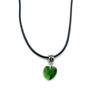 Macro detail of faceted green crystal heart pendant on black cord with ornate silver clasp
