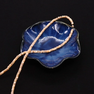 Dettaglio di perle in conchiglia naturale 2x4mm rosa e gialle su ciotola di ceramica blu