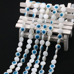 Macro detail of natural freshwater shell beads featuring blue evil eye designs for jewelry