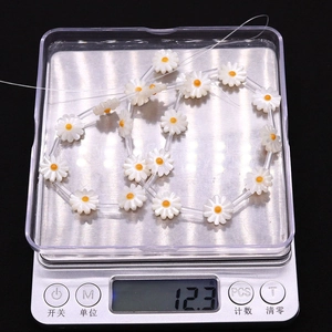 Macro detail of white daisy shell beads on a digital scale showing 12.3g product weight