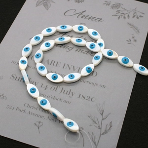 Macro shot of marquise shell evil eye beads arranged in a spiral on a grey invitation card