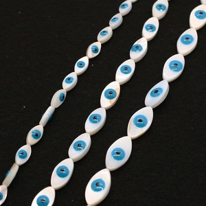 Macro view of marquise-shaped shell beads featuring blue evil eye patterns on black fabric