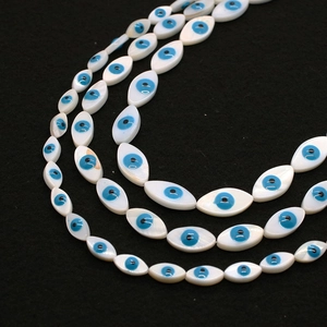 Macro shot of marquise shell beads featuring blue evil eye charms for jewelry making