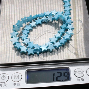 Makroaufnahme himmelblauer sternförmiger Perlmuschel-Perlen auf einer Digitalwaage mit 12,9g