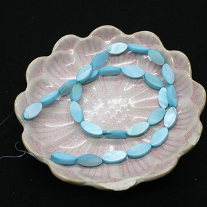 Perle ovali in conchiglia blu naturale su vassoio a petalo rosa con sfondo scuro