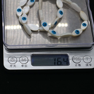 Macro detail of natural shell evil eye beads on a digital scale weighing 16.4 grams