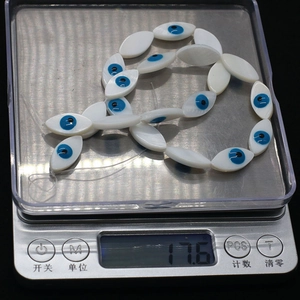 Detailed view of evil eye shell beads on a digital scale showing weight of seventeen grams
