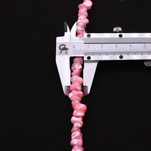 Détail de perles en coquillage rose naturel mesurées au pied à coulisse affichant 8,1 mm