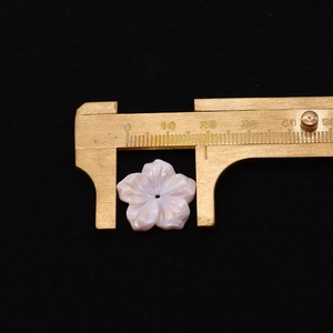 Macro shot of a 20mm carved pink shell flower bead with a brass caliper scale measurement