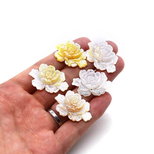 Natuurlijke lotus schelphangers in wit en geel getoond op een hand tegen een witte achtergrond
