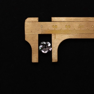 Macro view of 10mm flower-shaped natural black shell pendant measured with brass calipers