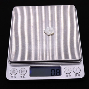 Makroansicht einer 10mm weißen Muschelblüte, die 0,8g Gewicht auf einer Digitalwaage zeigt