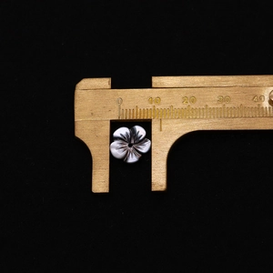 Gros plan d'une perle en nacre de 10mm en forme de fleur mesurée au pied à coulisse pour bijoux