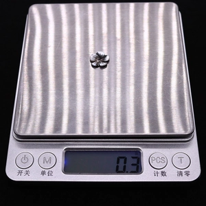 Vue macro d'un charm fleur en nacre noire sur une balance numérique affichant 0,3g
