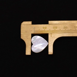 Macro shot of heart-shaped white mother of pearl bead measured by brass caliper