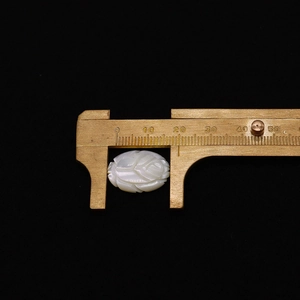 Macro shot of a 15x20mm white shell rose carving being measured with a brass caliper