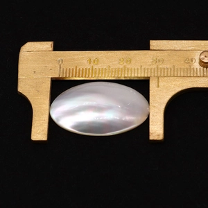 Macro shot showing measurement of a polished white oval mother of pearl shell bead
