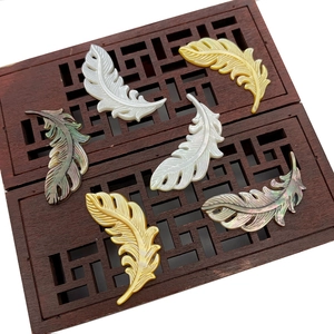 Détail de pendentifs plumes en nacre naturelle avec textures sculptées et reflets irisés