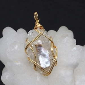 Macro detail of handmade gold wire wrapped natural pearl and crystal pendant on white stone