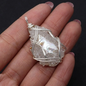 Macro shot of silver wire-wrapped pendant with baroque pearl and white teardrop crystal