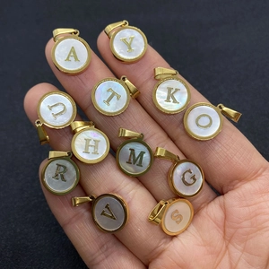 Pendentifs alphabet ronds en nacre avec cadre doré présentés dans la main ouverte