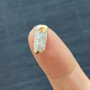 Irregular freshwater pearl pendant with gold border displayed on a fingertip for scale