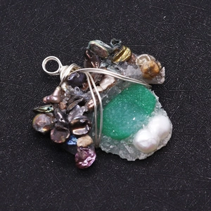 Macro shot of handmade pendant with green stone, white pearls, and irised shell fragments
