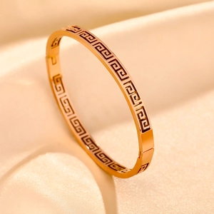 Macro shot of gold stainless steel bangle with Greek key engraving on apricot satin fabric