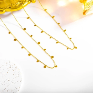 Close-up of a 18k gold plated geometric disk tassel necklace on a textured stone surface