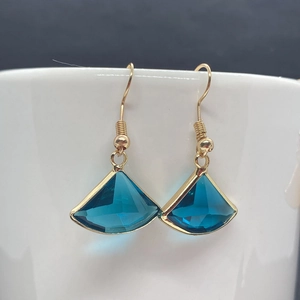 Primer plano de pendientes de cristal azul en forma de abanico con borde dorado