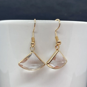 Macro detail of fan-shaped natural stone gold earrings displayed on a white ceramic rim