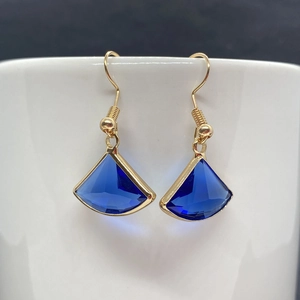 Macro view of gold-plated fan-shaped earrings featuring faceted dark blue stones