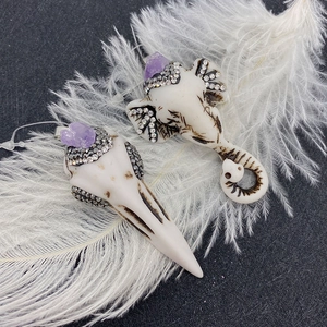 Elephant and skull carved pendants with purple crystals and rhinestones on a feather background