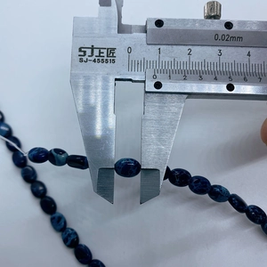 Close-up measurement of 7x9mm oval imperial stone beads with blue marble texture