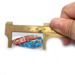 Makroaufnahme eines 37mm Tropfenstein-Anhängers mit roter und blauer Textur auf einem Messschieber