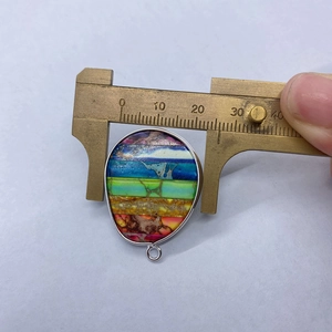 Width measurement of teardrop emperor stone pendant using brass calipers on white background