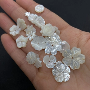 Macro shot of hand holding white natural shell flower charms for DIY jewelry making