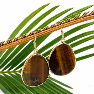 Detailed view of natural tiger eye drop earrings with gold edging on a wooden branch