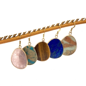 Five pairs of teardrop natural stone earrings in rose quartz and tiger eye on a wooden branch