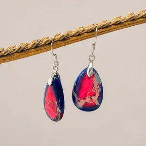 Macro shot of teardrop-shaped turquoise earring with pink and blue textures on a branch
