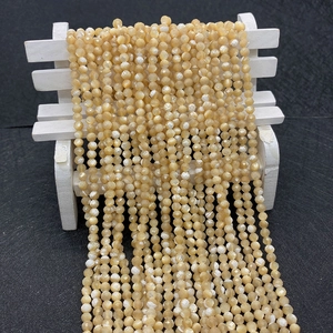 Close-up of 2-3mm faceted natural cream shell beads arranged on a small white wooden bench