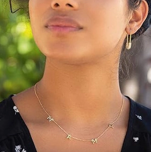 Detailopname van de gouden MAMA ketting en kristallen veiligheidsspeld oorbel op model
