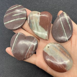 Detail of natural striped agate pendants in heart and water drop shapes held in hand
