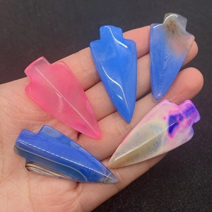 Dettaglio di cinque ciondoli in agata a forma di punta di freccia tenuti in mano