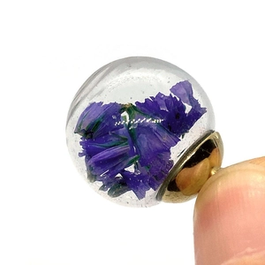 Macro view of handmade glass ball pendant filled with purple dried flowers and gold base