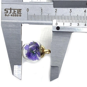 Macro shot showing 16mm diameter measurement of round glass ball pendant with purple flowers
